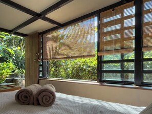 A room with a bed, rolled towels, and a window with bamboo blinds. - Casa Nanita | Chirripó riverfront mountain retreat (Perez Zeledon)