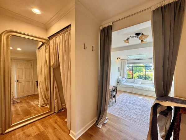 A hallway with a large mirror, a door, and a view into a living area with a sofa and a window. - Quiet studio oasis in desirable Laurelhurst neighborhood (Seattle)