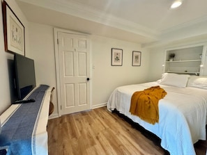 A bedroom with a bed, a television, a door, and framed pictures on the wall. - Quiet studio oasis in desirable Laurelhurst neighborhood (Seattle)