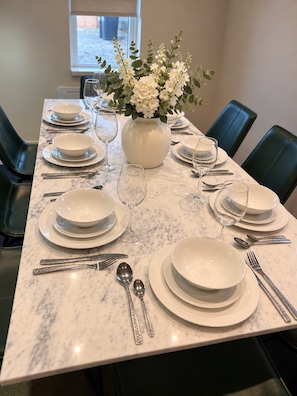 A dining table set with white plates, bowls, and cutlery, centered with a vase of white flowers. - Burton House|4 Bed|Sleeps8|Private Parking (Wool)