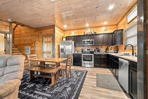 A compact kitchen with wooden walls, a dining area with a table and chairs, and modern appliances. - Cozy Cabin Near Dollywood & Pigeon Forge w/ Hot Tub (Sevierville)
