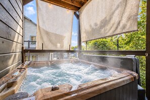 Ein Whirlpool mit Holzverkleidung, umgeben von einer Holzdielen-Terrasse, mit einem Haus im Hintergrund.