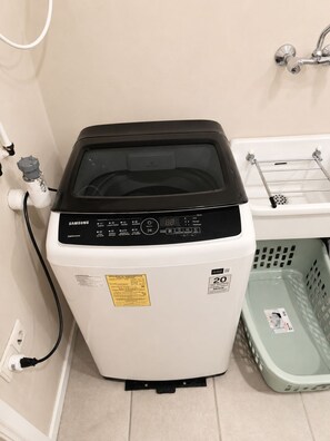 A Samsung washing machine in a bathroom with a white sink and a green laundry basket. - Spacious ground-floor apartment with an ocean-view pool and the beach within walking distance (Willemstad)