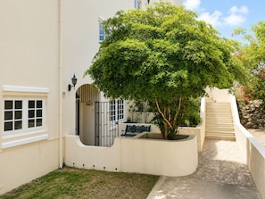A building with a white exterior, a tree in a planter, a gate, and a staircase. - Spacious ground-floor apartment with an ocean-view pool and the beach within walking distance (Willemstad)