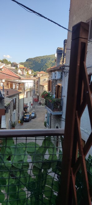 A residential area with stone buildings, a narrow street, and a view of a hilly landscape. - Waking up and looking out at the mountains, then heading down to the square for breakfast (Licenza)
