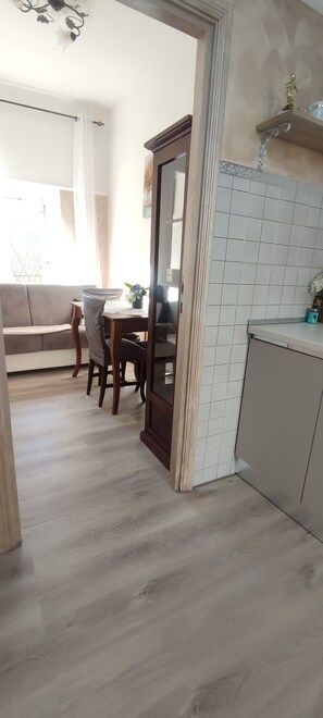 A modern kitchen with white cabinets, a dining area with a wooden table and chairs, and a view of a living room with a sofa and a window. - Waking up and looking out at the mountains, then heading down to the square for breakfast (Licenza)