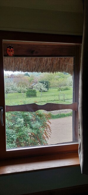 A window with a wooden frame and a thatched roof, overlooking a garden with various plants and a fence. - Country Cottage - A Quiet Norman Thatched Cottage Close to Nature (Marais-Vernier)