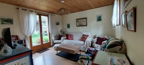 A cozy living room with a sofa, a coffee table, and a television on a wooden table. - Country Cottage - A Quiet Norman Thatched Cottage Close to Nature (Marais-Vernier)