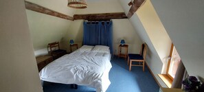 A bedroom with a bed, two chairs, a table, a window with curtains, and exposed wooden beams. - Country Cottage - A Quiet Norman Thatched Cottage Close to Nature (Marais-Vernier)