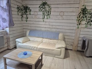 Ein Zimmer mit einem beigefarbenen Sofa, einem Holztisch mit einer blauen Schüssel und Pflanzen an den Wänden.
