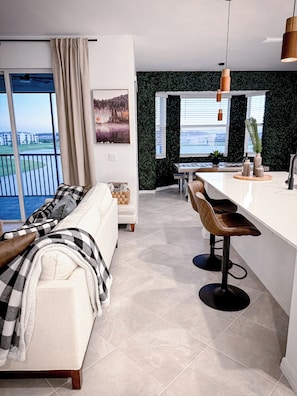 Una sala de estar moderna con un sofá, un comedor con mesa y sillas, y una cocina con barra.