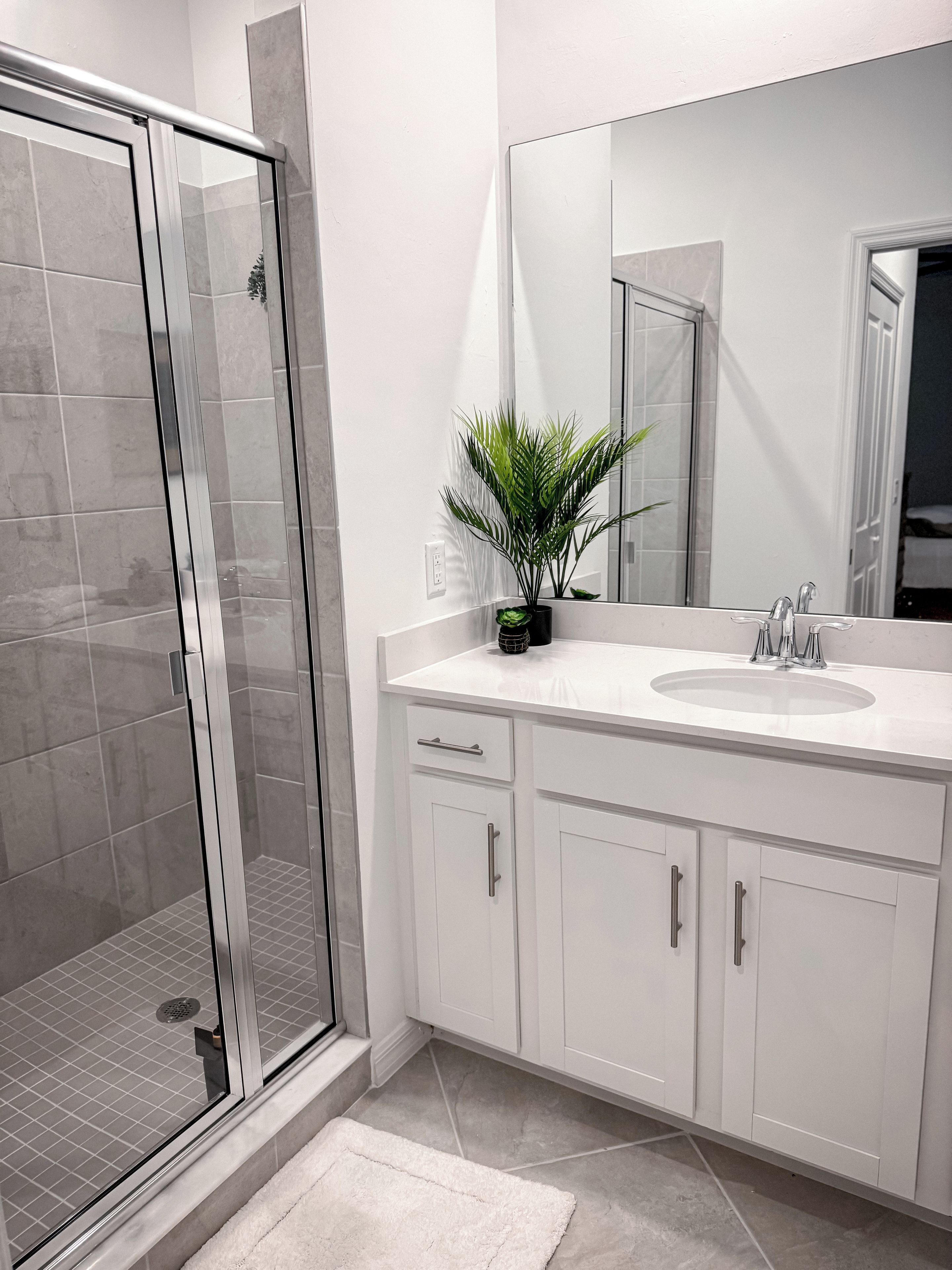Un baño moderno con cabina de ducha de vidrio, un lavabo blanco con espejo y una planta en maceta.