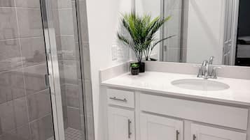 Un baño moderno con cabina de ducha de vidrio, un lavabo blanco con espejo y una planta en maceta.