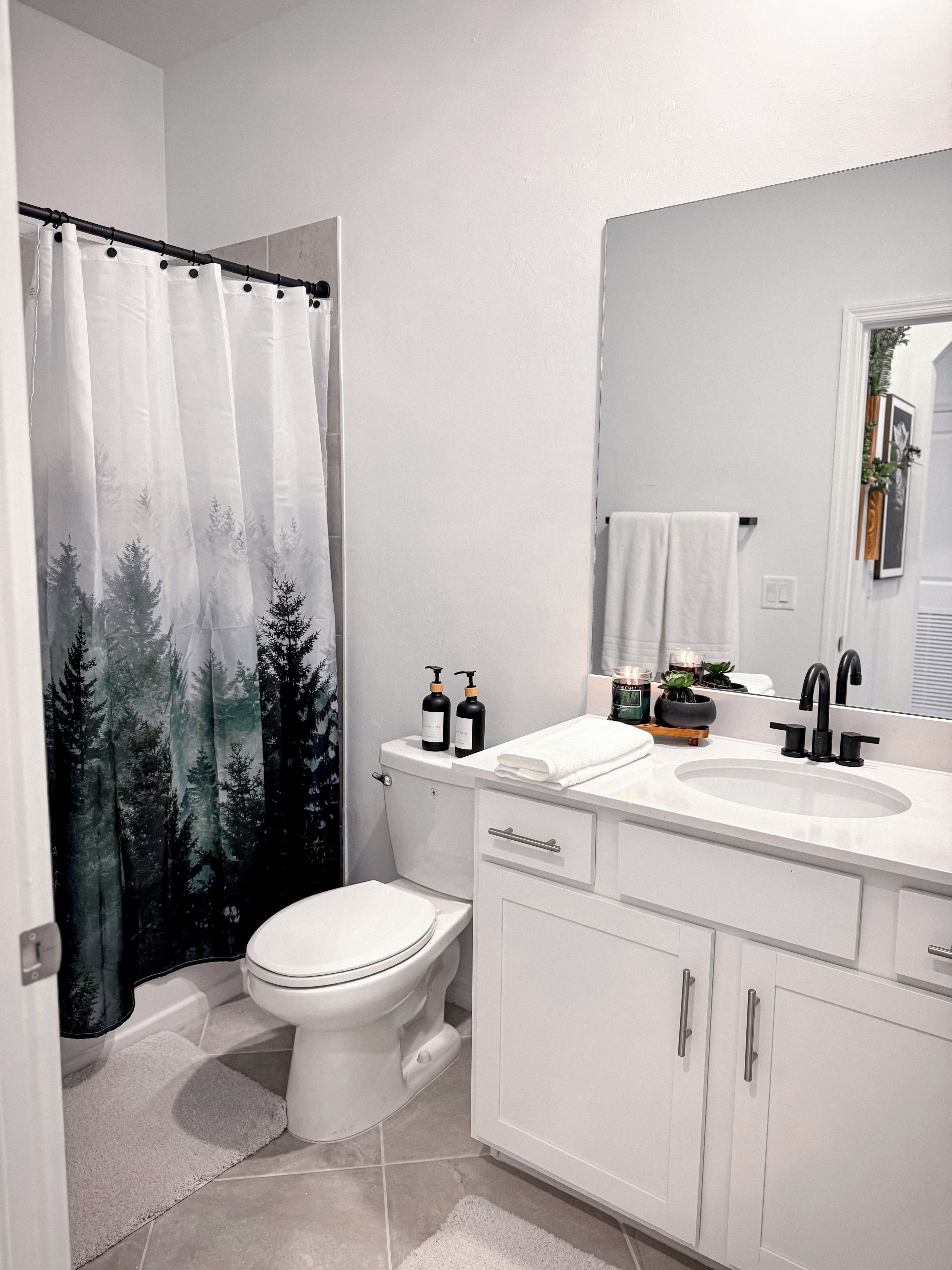 A modern bathroom with a toilet, sink, and shower curtain featuring a forest scene.