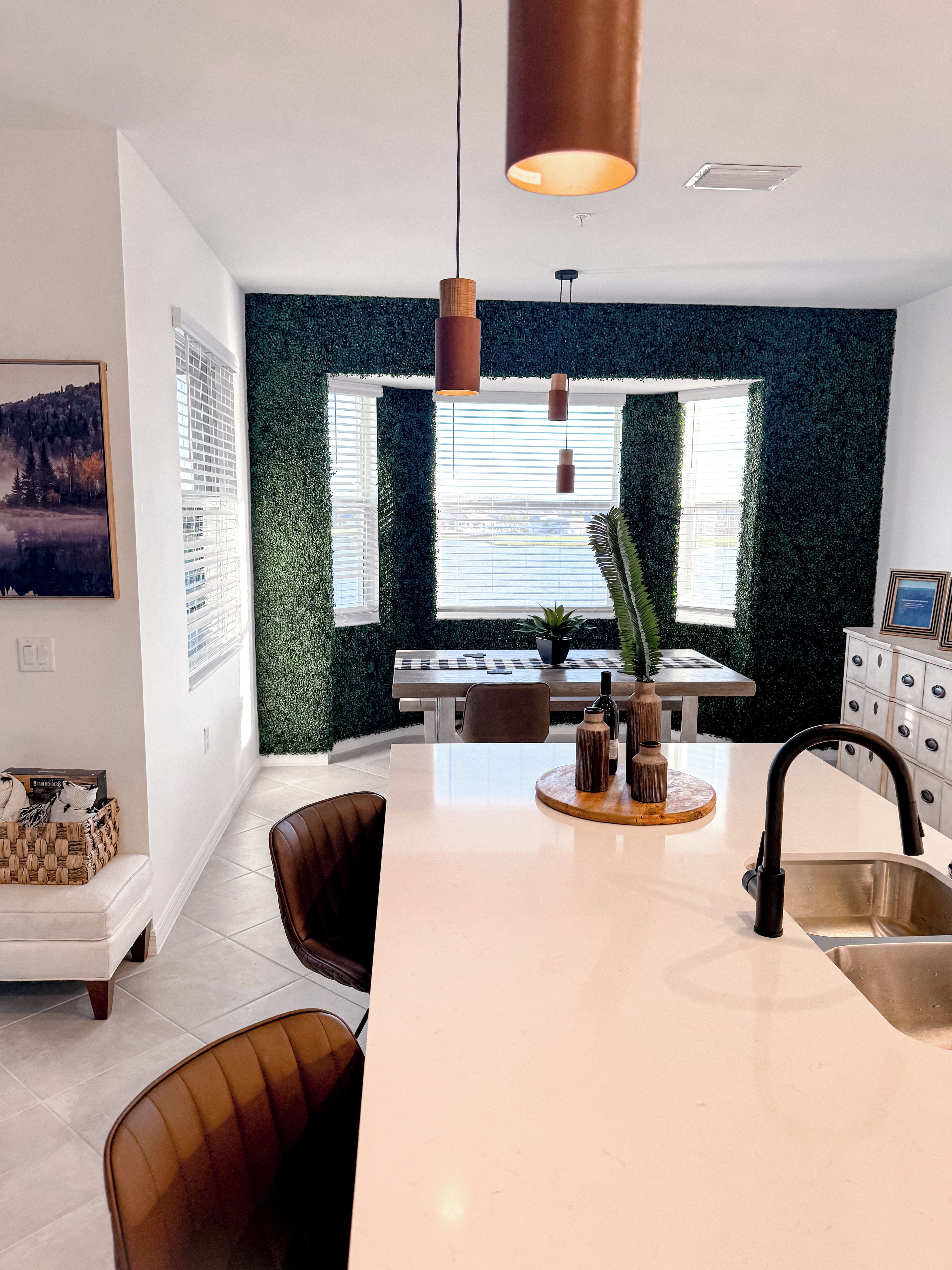 A modern kitchen with a central island, pendant lighting, and a view through a window with blinds.