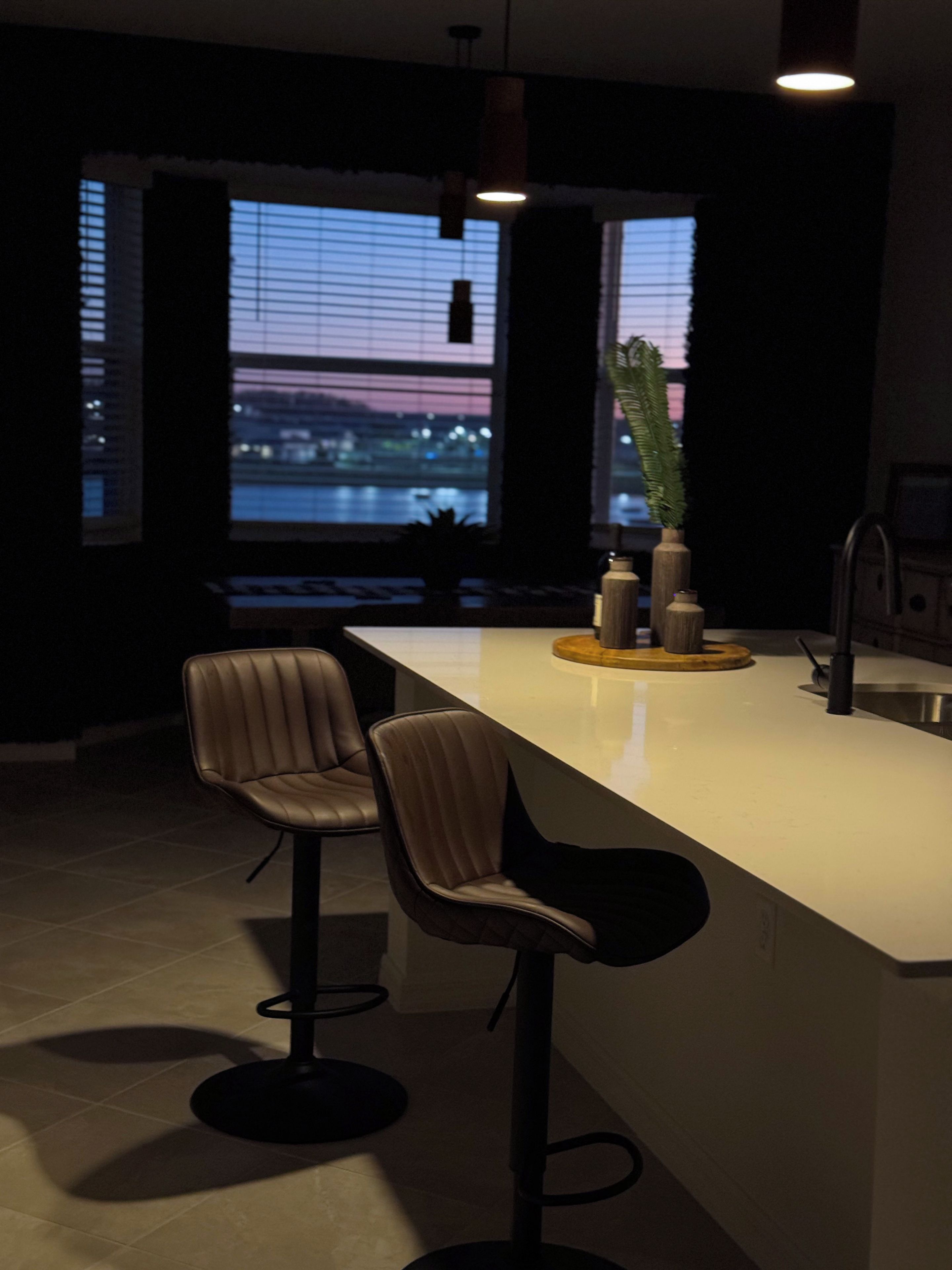 Una cucina moderna con angolo bar, due sgabelli da bar, una pianta in vaso e vista sulla città attraverso ampie finestre.