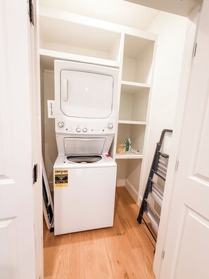 A compact laundry room with a front-loading washer and dryer, wooden flooring, and built-in shelving. - Homewood Luxury 2 Bedroom 2.5 Bath Townhome 3018 (Homewood)