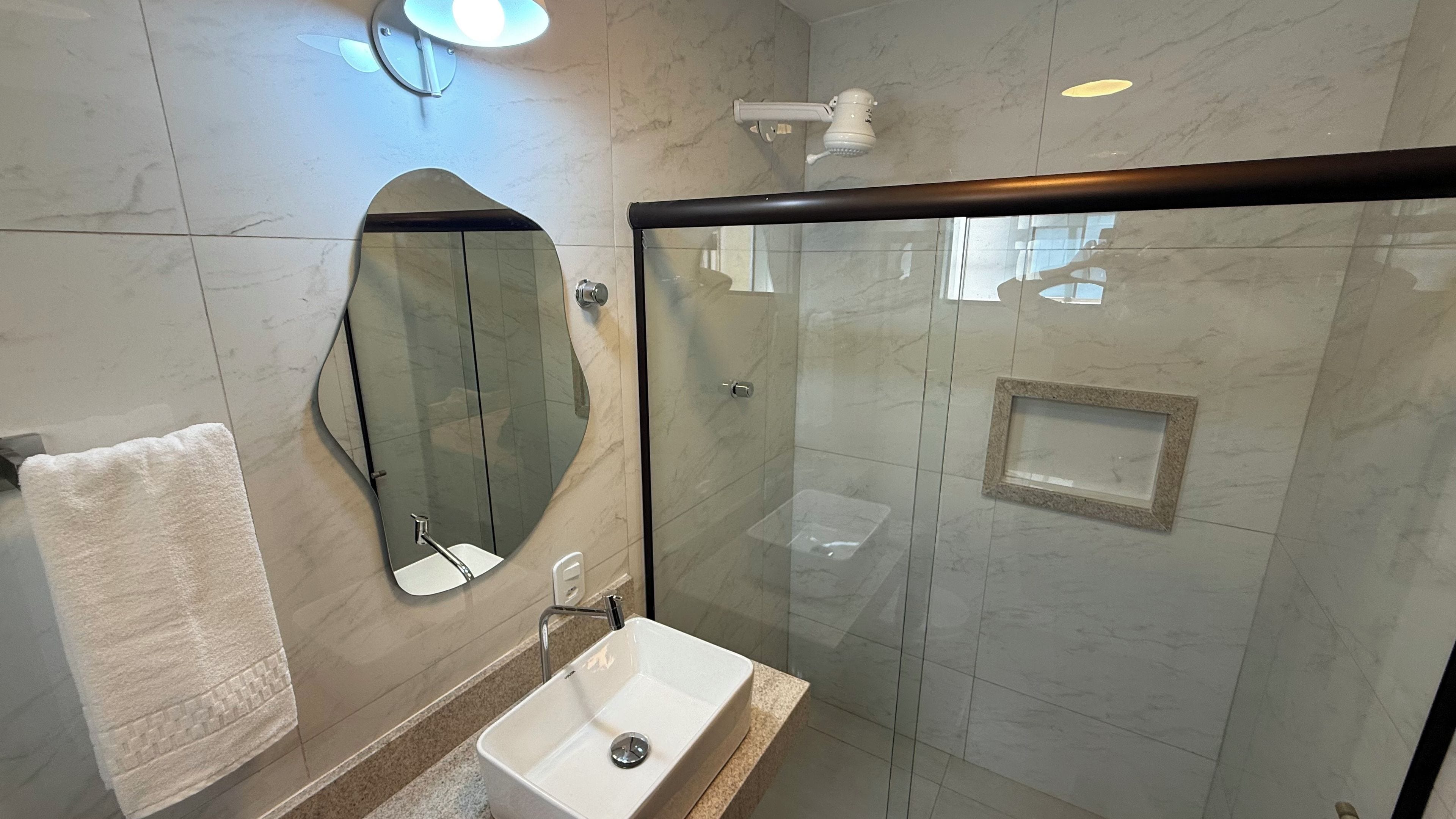 A modern bathroom with a glass-enclosed shower, a white sink, and a large mirror.