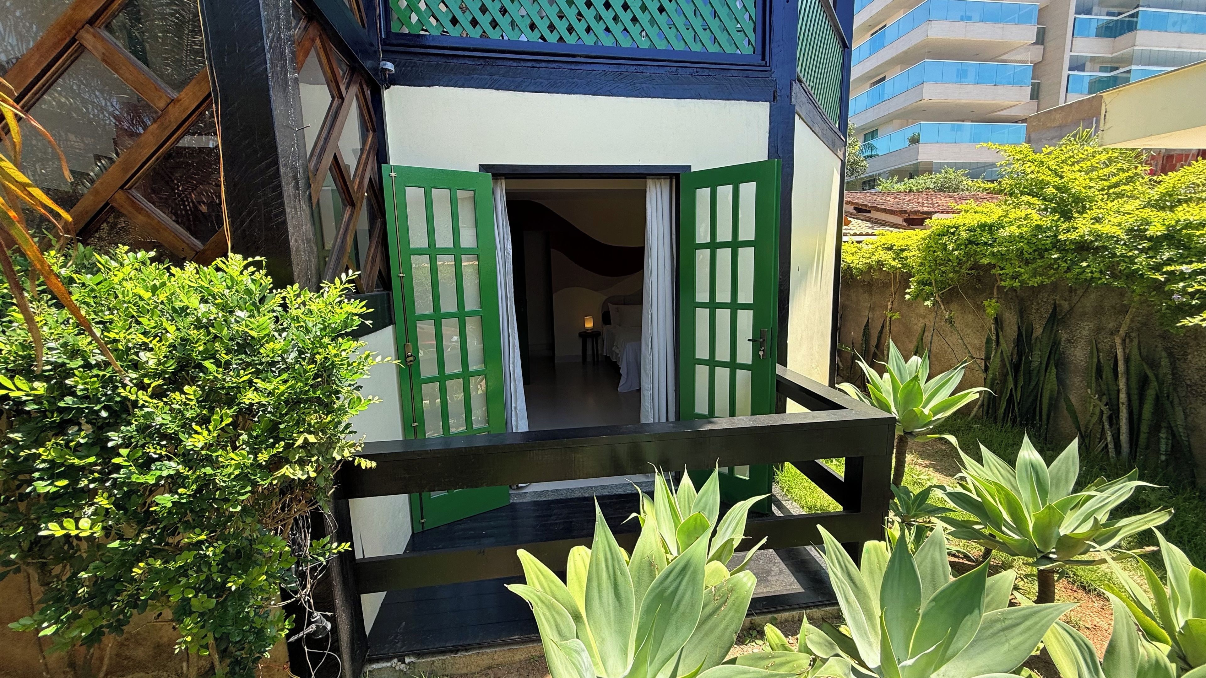 A building with a green door and a balcony, surrounded by greenery.