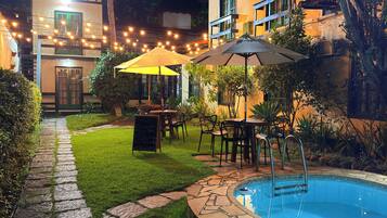 A poolside area with a stone pathway, outdoor seating, and a building with a tiled roof.