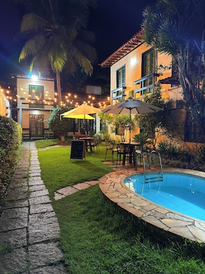 A poolside area with a stone pathway, outdoor seating, and a building with a tiled roof.