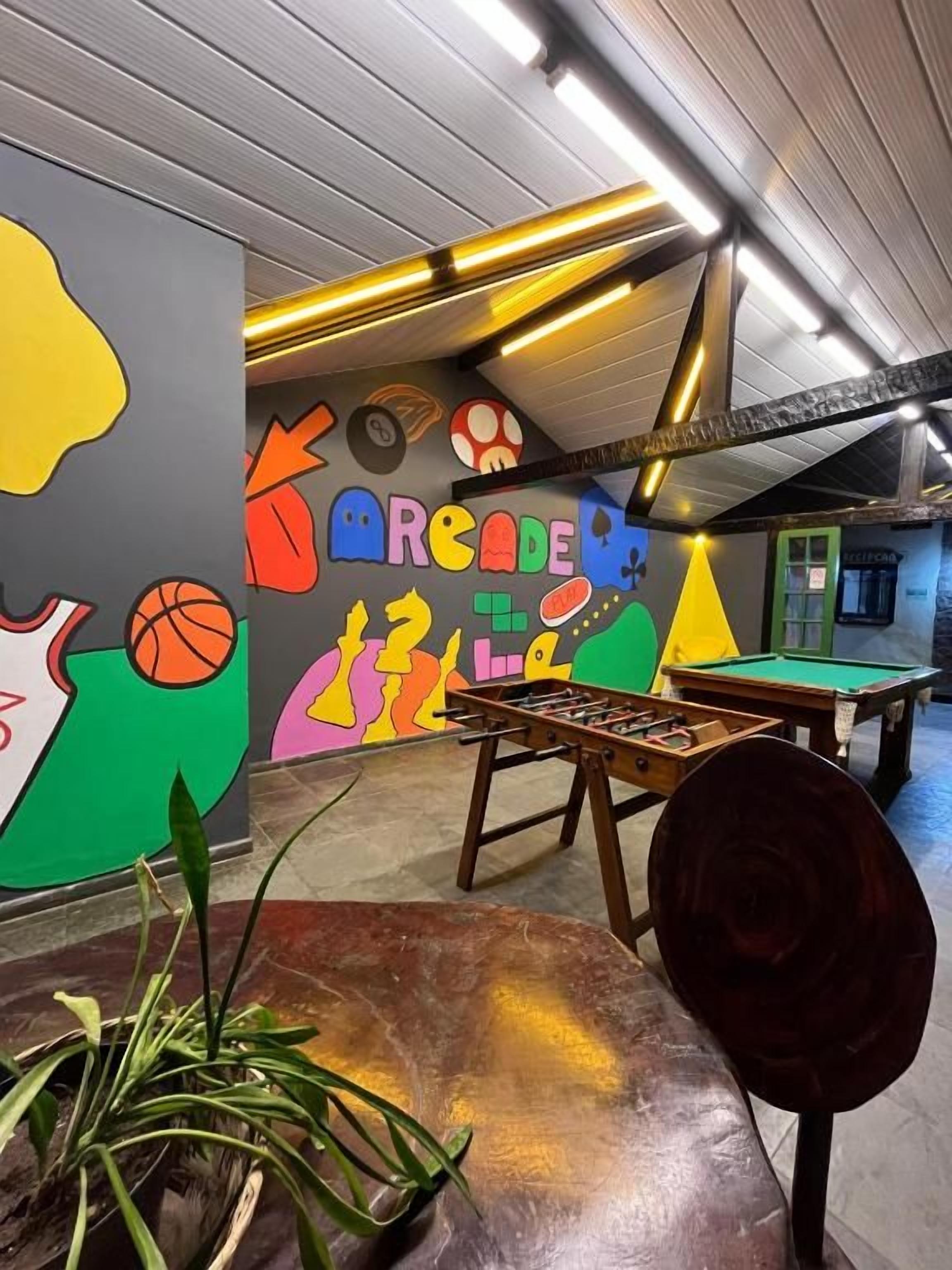 A billiards room with a pool table, a foosball table, and a colorful mural on the wall.