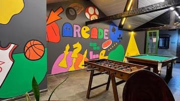 A billiards room with a pool table, a foosball table, and a colorful mural on the wall.