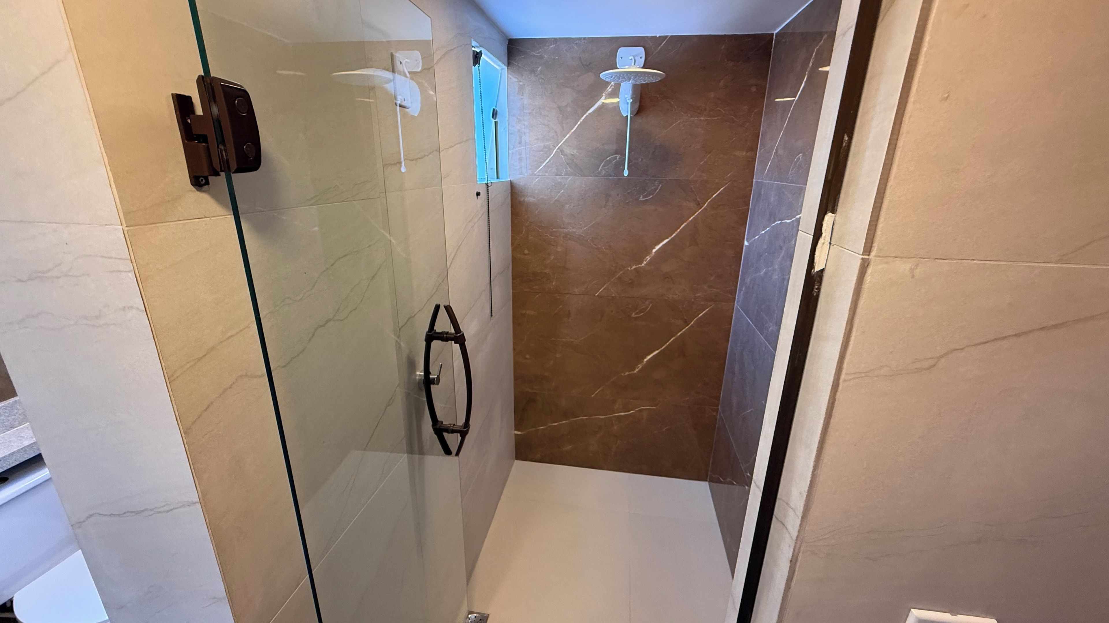 Een douche met glazen wand, een handdouche en een kraan op de muur.