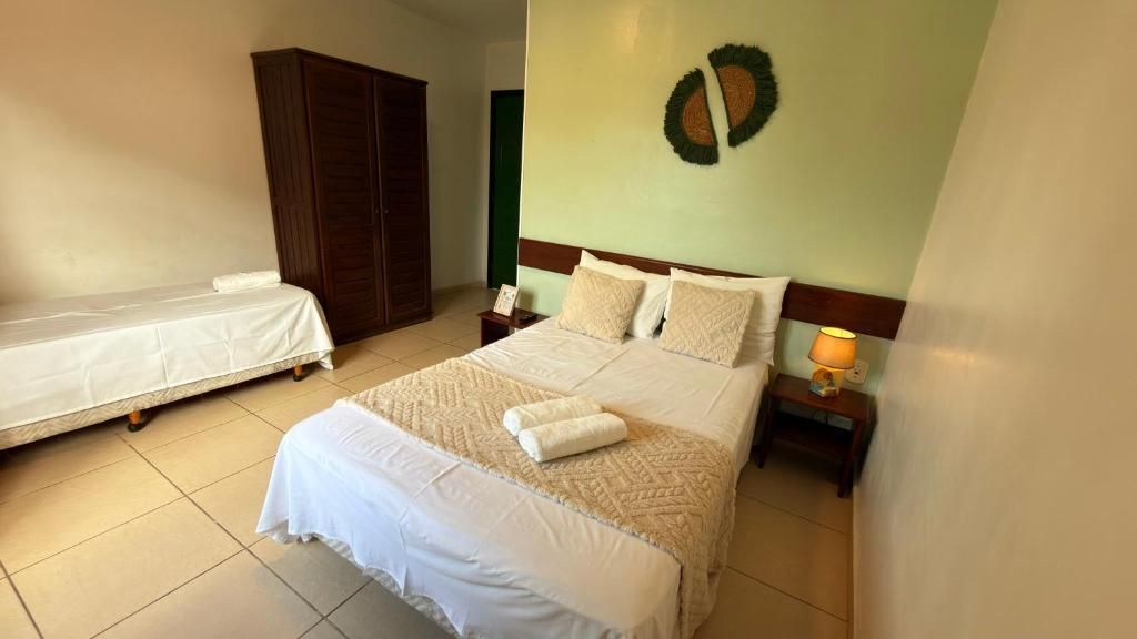 A bedroom with a large bed, a smaller bed, a wardrobe, a nightstand with a lamp, and a wall decoration.