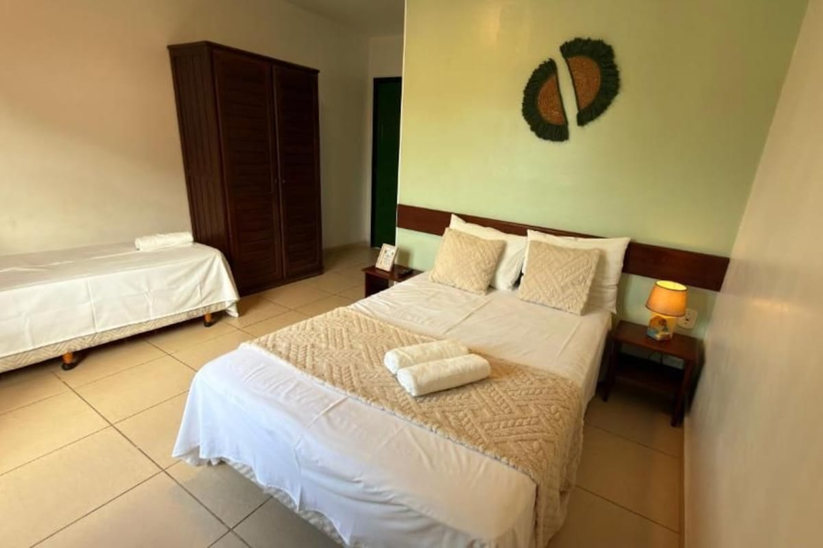 A bedroom with a large bed, a smaller bed, a wardrobe, a nightstand with a lamp, and a wall decoration.