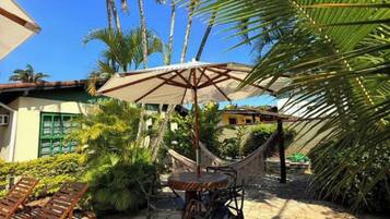 Eine Terrassenfläche mit einer Hängematte, Liegestühlen und einem Tisch unter einem großen Sonnenschirm.