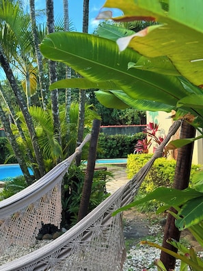 A hammock in a lush garden with a pool and tropical plants.