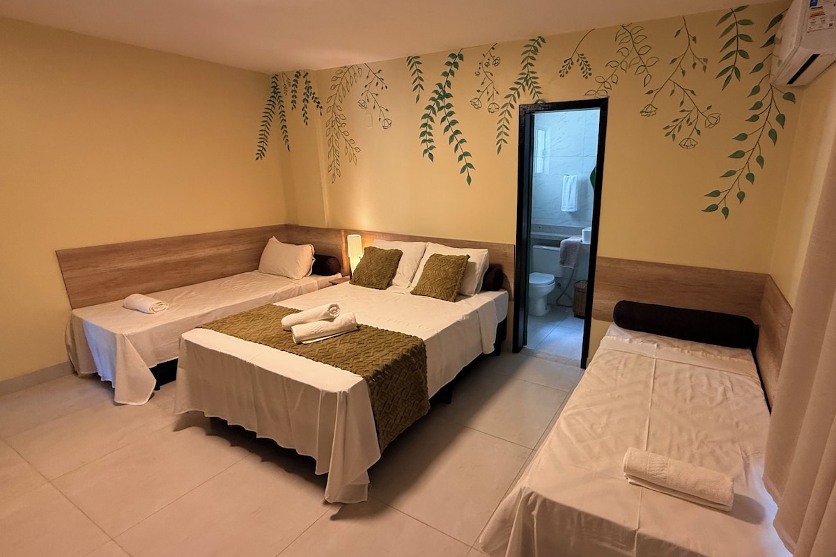 Habitación de hotel con dos camas, cabecero de madera, baño visible a través de una puerta de cristal y una pared con motivos de hojas.