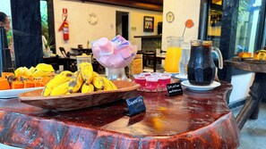 A breakfast buffet with various fruits, a bowl of bananas, and a pitcher of iced coffee.
