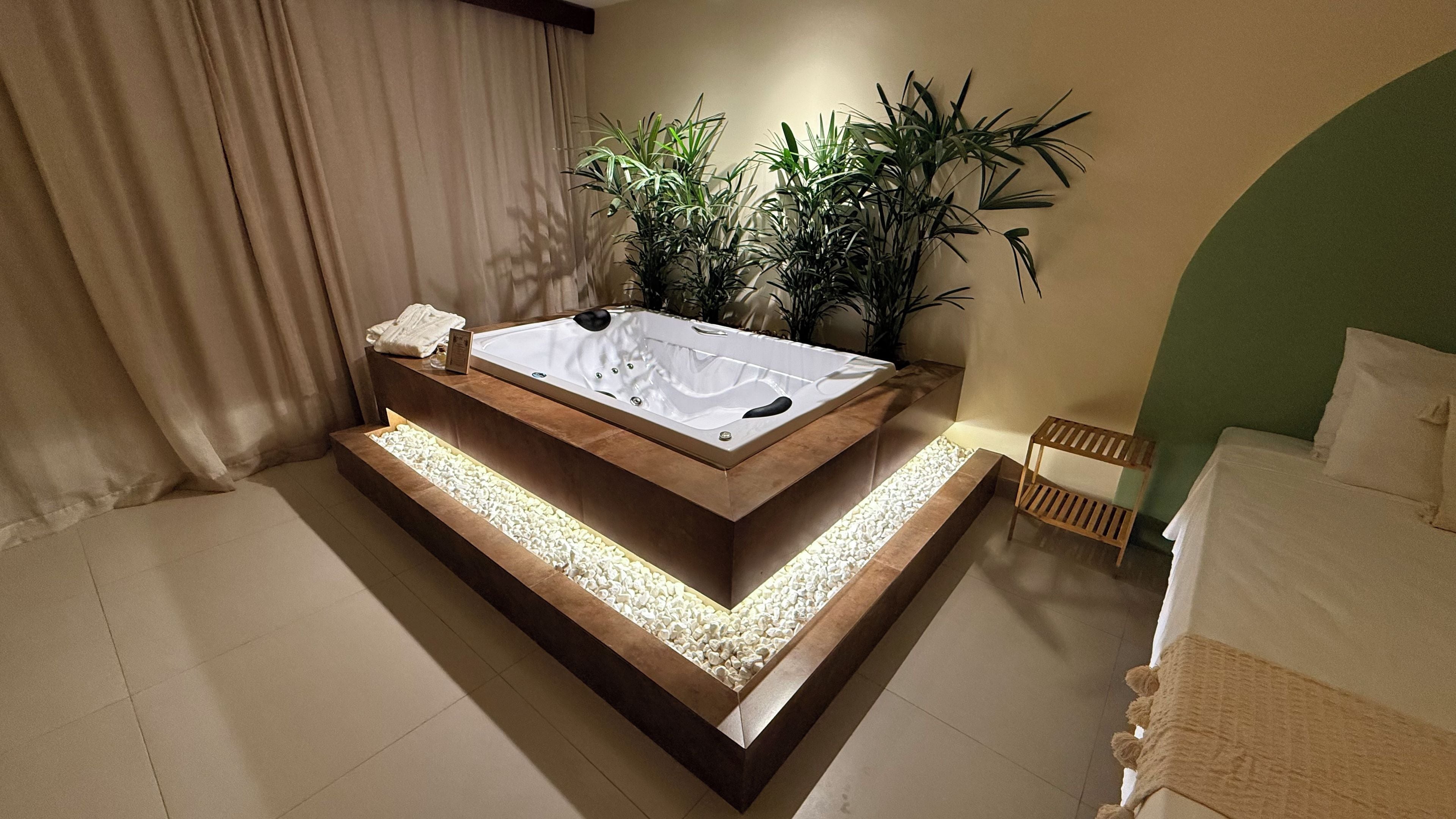 A modern bathroom with a freestanding bathtub, a small wooden bench, and a potted plant.