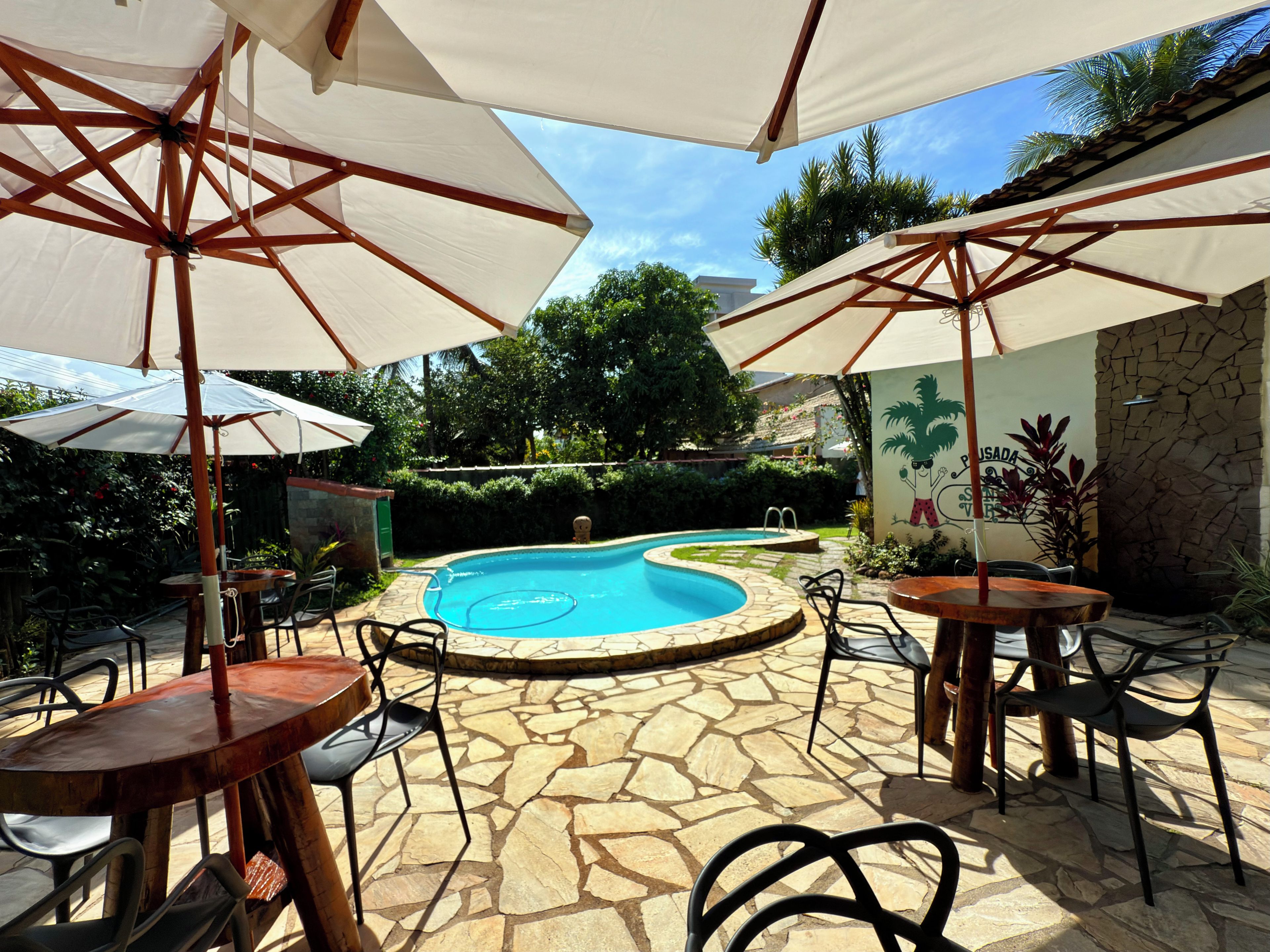 Zona de piscina amb paviment de pedra, seients exteriors i ombrelles.