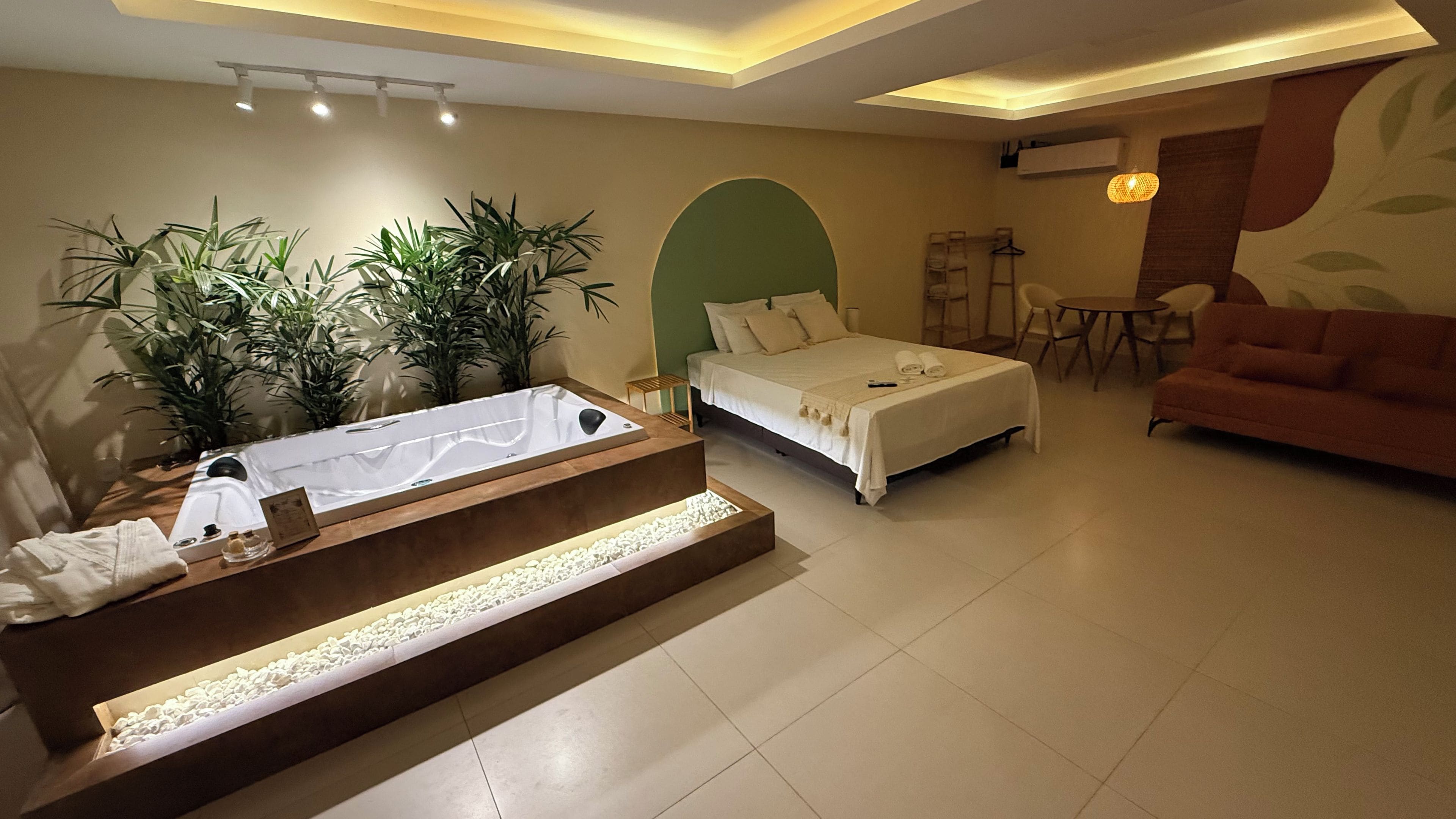 A modern hotel room with a bed, a sofa, a small table, and a bathtub with a wooden bench.