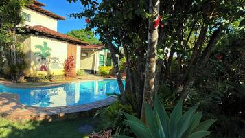 A pool surrounded by lush greenery and a building with a tiled roof.
