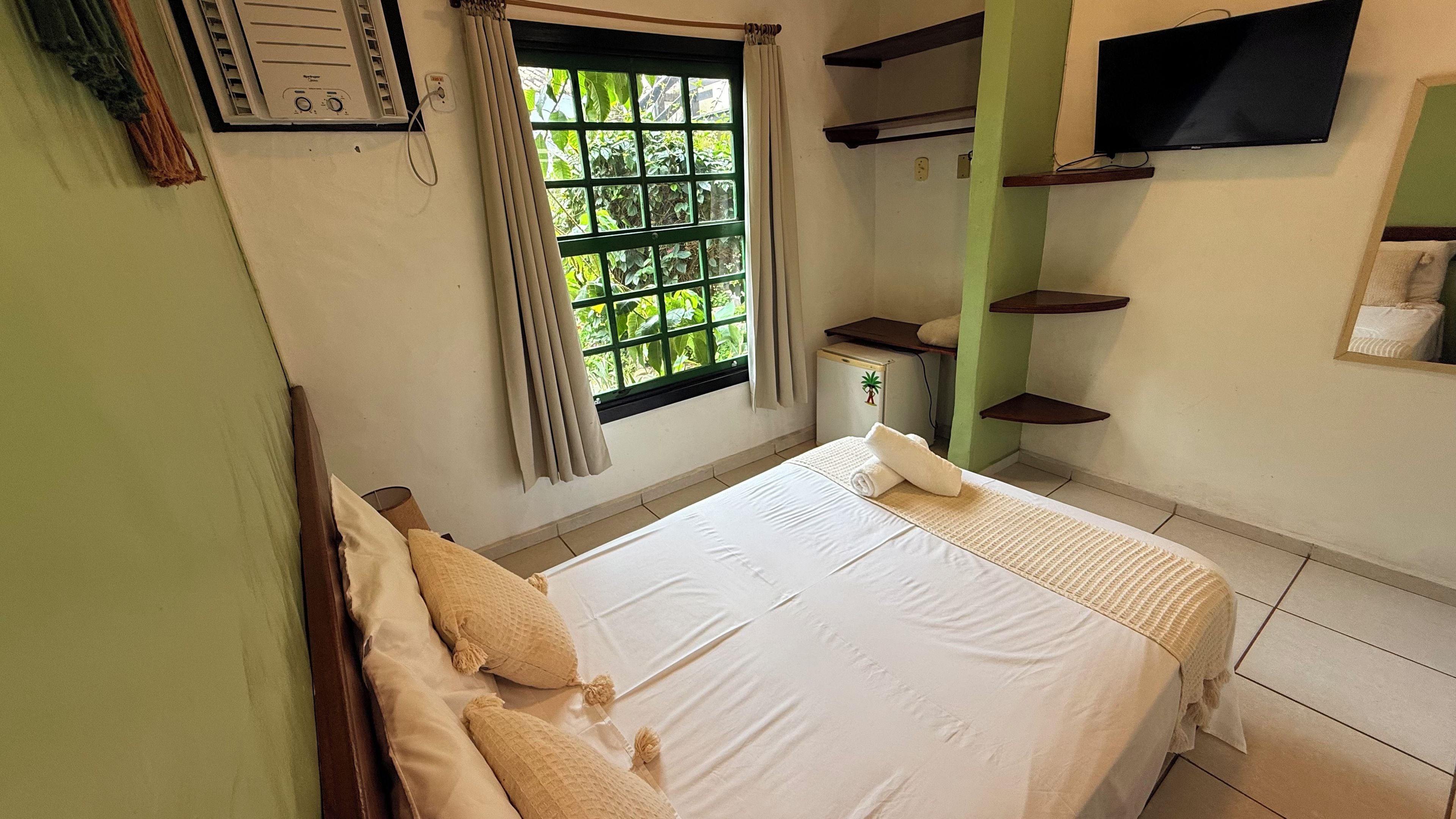 A hotel room with a bed, a window with curtains, a small TV, and a wall-mounted heater.