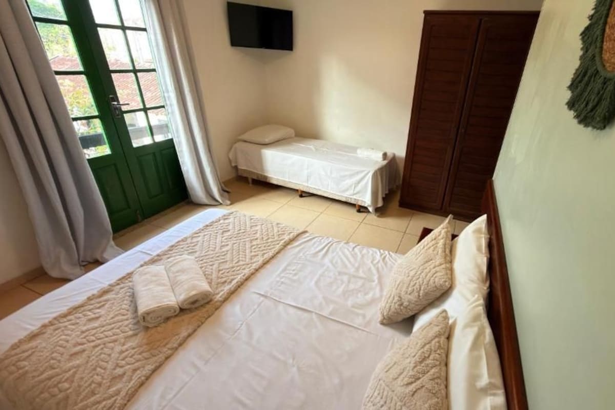 Un dormitorio con una cama grande, una cama más pequeña, un armario y un televisor en la pared.