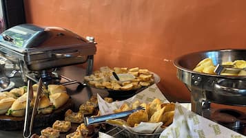 A buffet table with various food items, including sandwiches, fried items, and a bowl of chips.