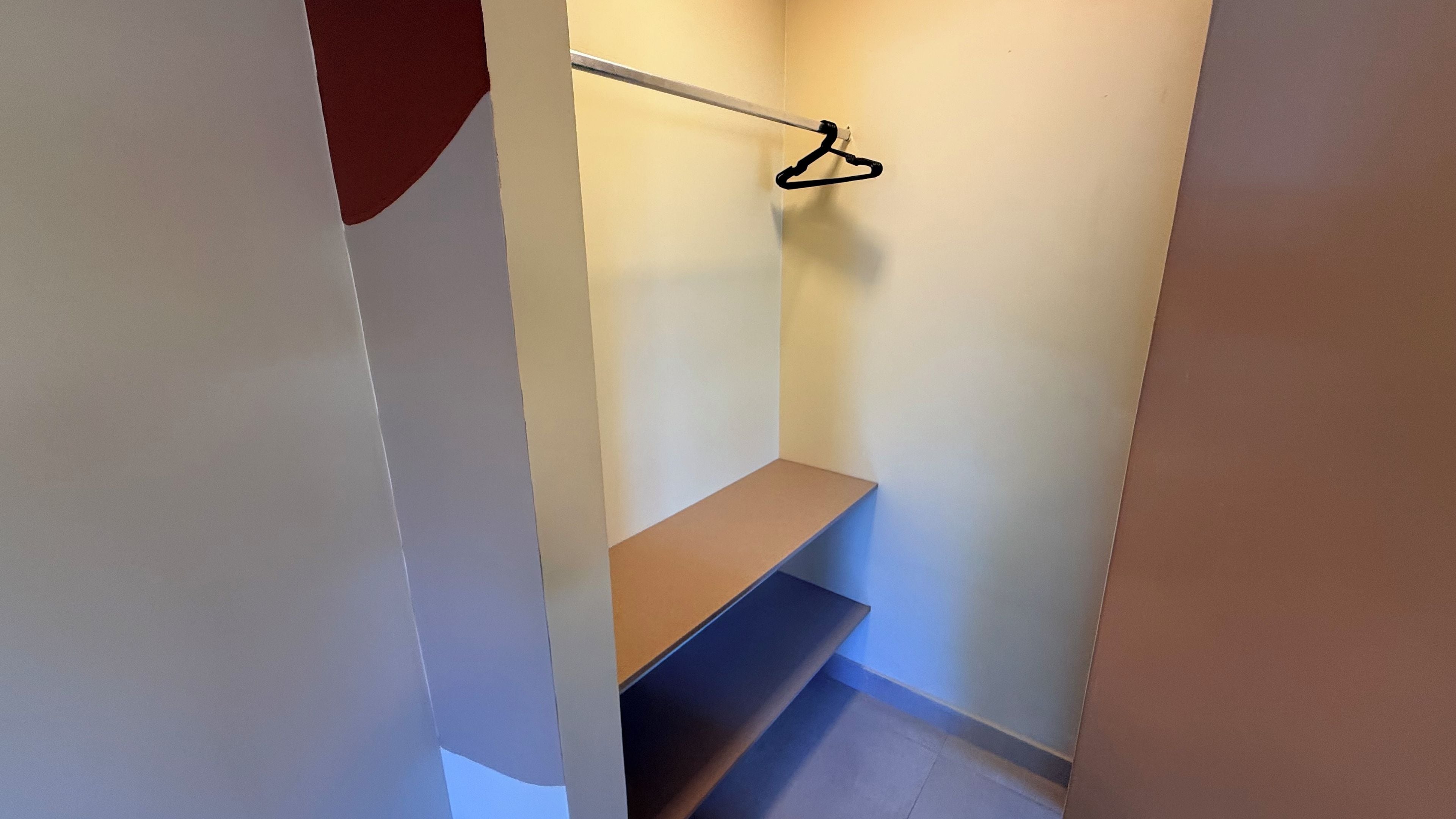 Un pasillo estrecho con un estante de madera y un perchero negro sobre una pared blanca.