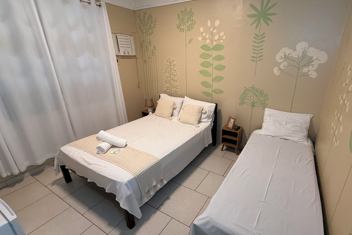 Un dormitorio con una cama doble, una cama individual y una mesita de noche con una lámpara.