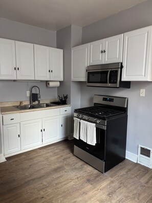 A kitchen with white cabinets, a stainless steel stove, a microwave, and a sink. - Quaint 2-bedroom house in Detroit perfect for your getaway (Detroit)