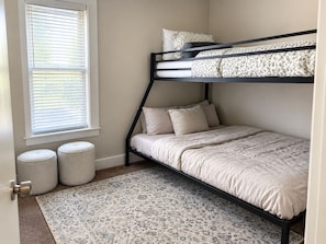 A bunk bed with a headboard, a window with blinds, two round ottomans, and a patterned rug. - Quaint 2-bedroom house in Detroit perfect for your getaway (Detroit)