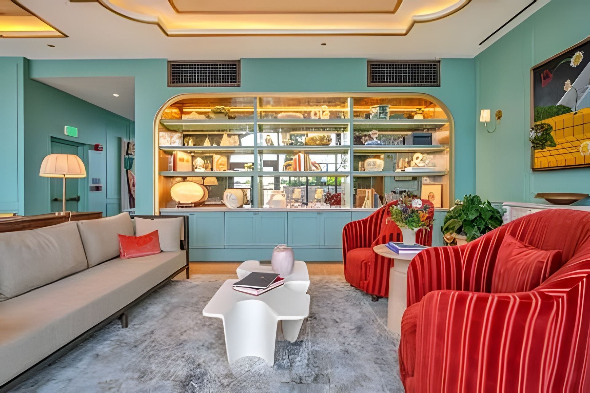 Un intérieur moderne avec un canapé, des fauteuils rouges, une table basse et une vitrine contenant divers objets.