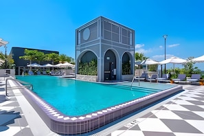 Piscina com estrutura de edifício moderno, espreguiçadeiras e guarda-sóis.