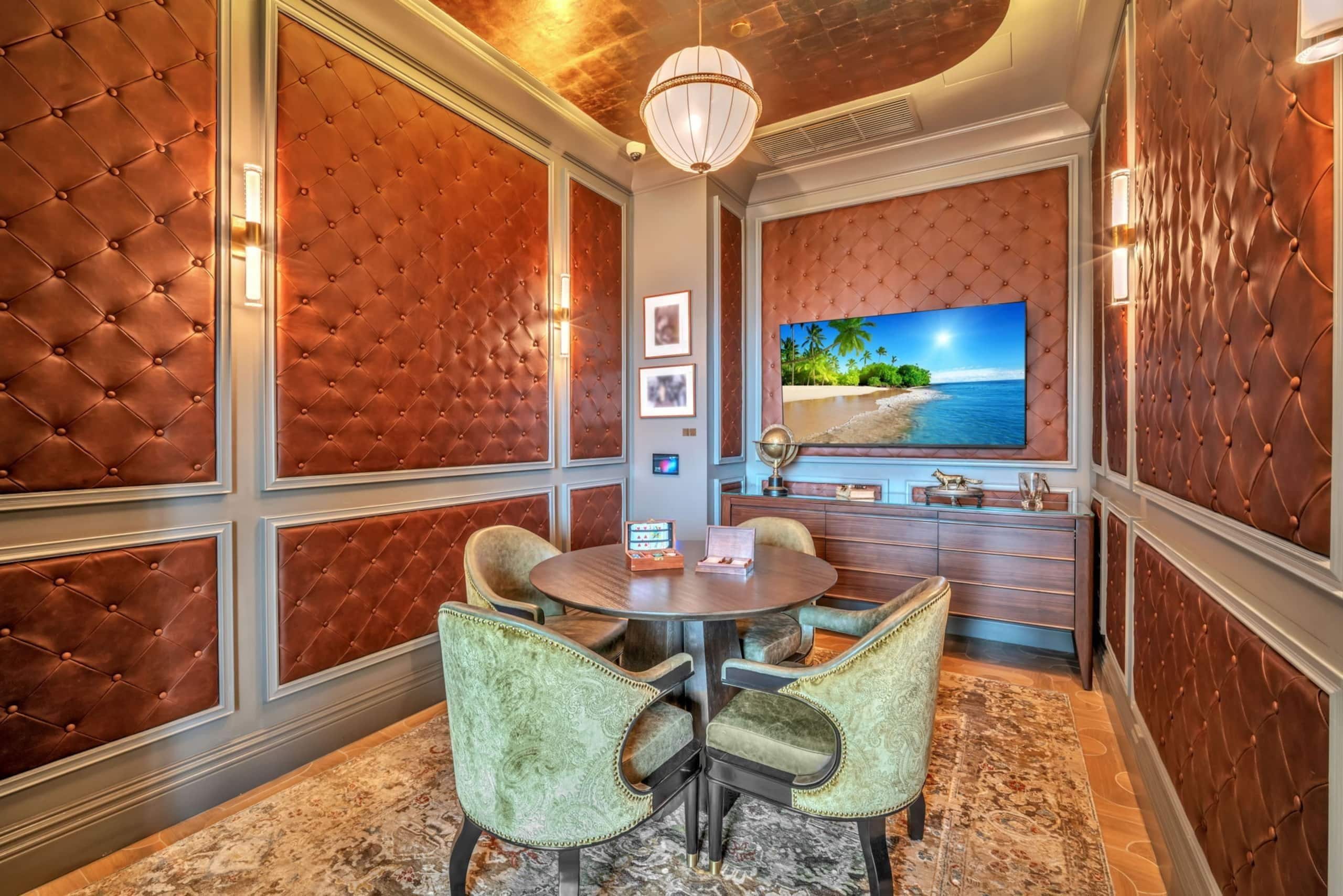 Une pièce avec un grand téléviseur fixé au mur, une table ronde entourée de chaises et un tapis à motifs.