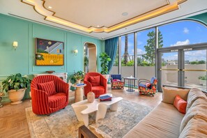 A modern living room with a sofa, armchairs, and a coffee table. There is a large window with a view of the city.