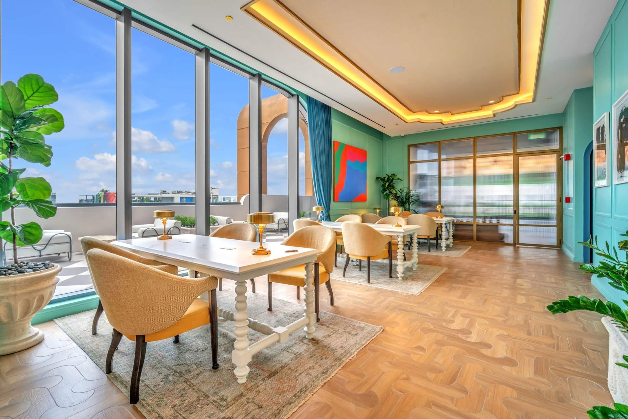 Un comedor moderno con ventanas amplias, vistas a la ciudad y un cuadro abstracto y colorido.